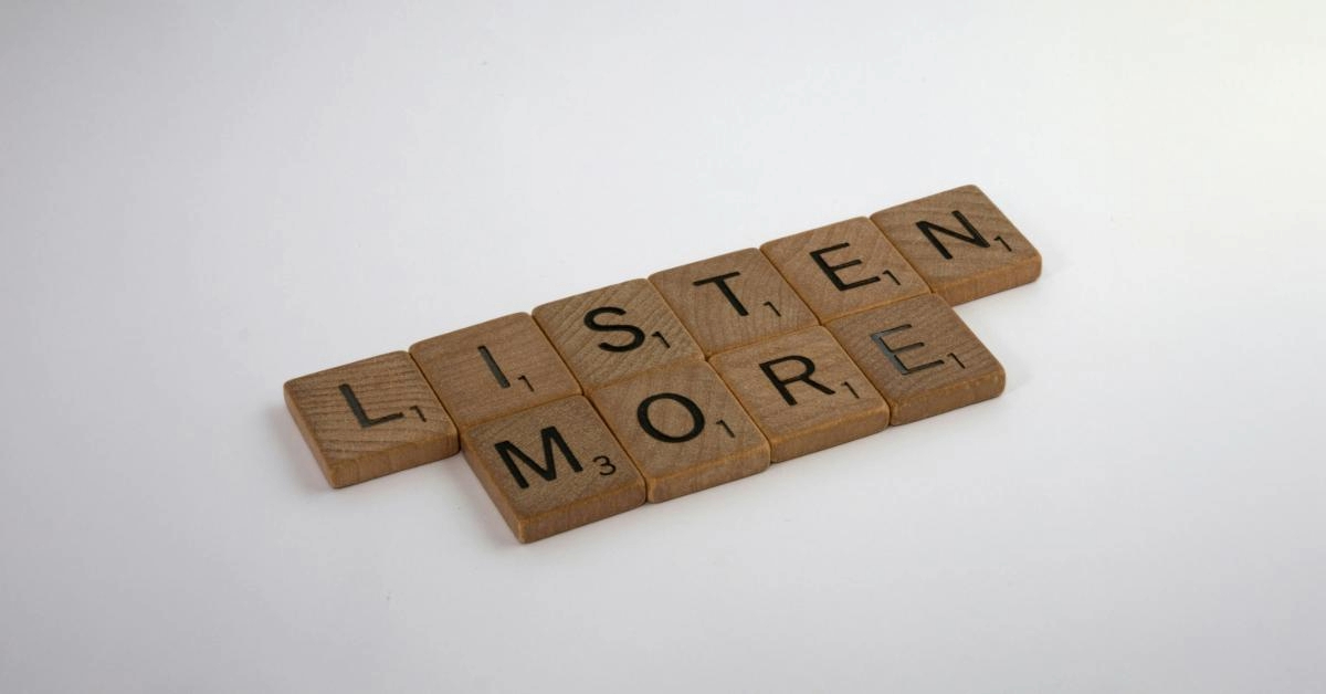 Scrabble tiles spelling out listen more, situated diagonally.