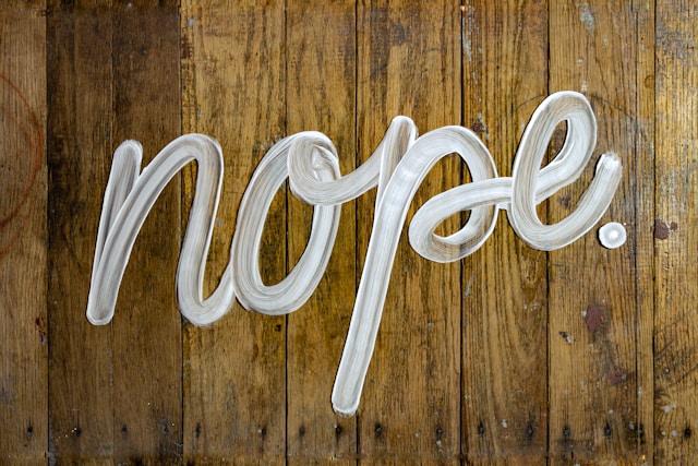 The word "Nope" appears in a cursive font against a wood-grain background.