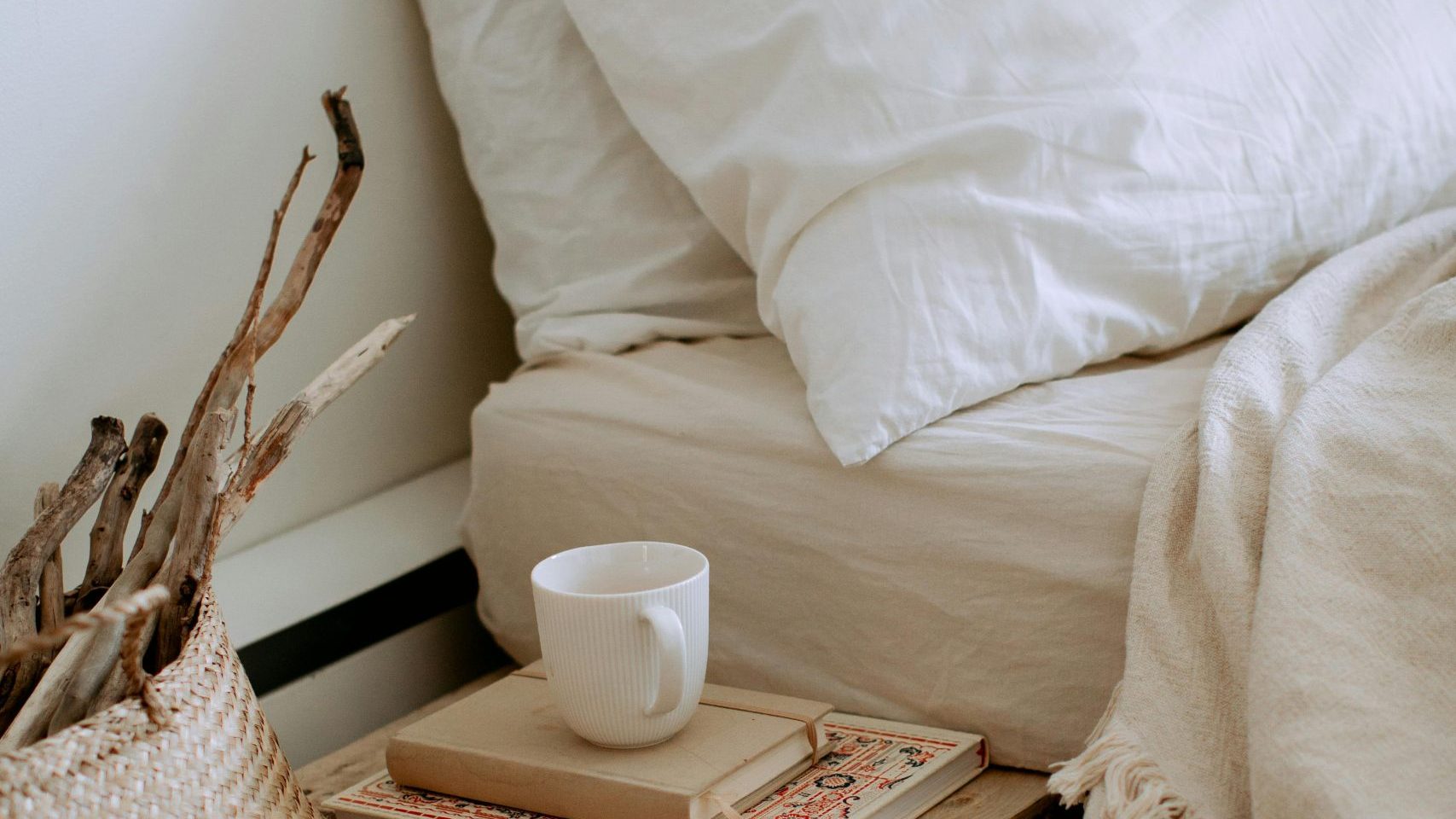 A coffee cup sits on a nightstand next to a bed with the covers turned down.