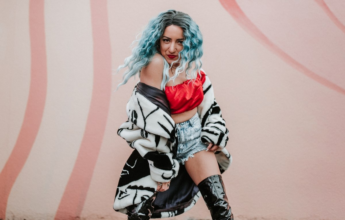 Girl with blue hair dancing in a red top and black and white jacket