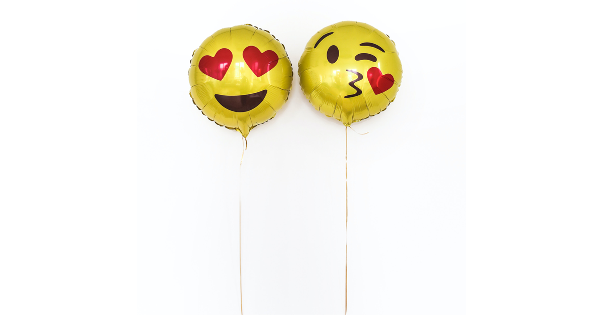 Two balloons with emoji faces. The balloon the left is the Smiling Face with Heart-Eyes Emoji. The emoji on the right is the Face Blowing a Kiss Emoji.