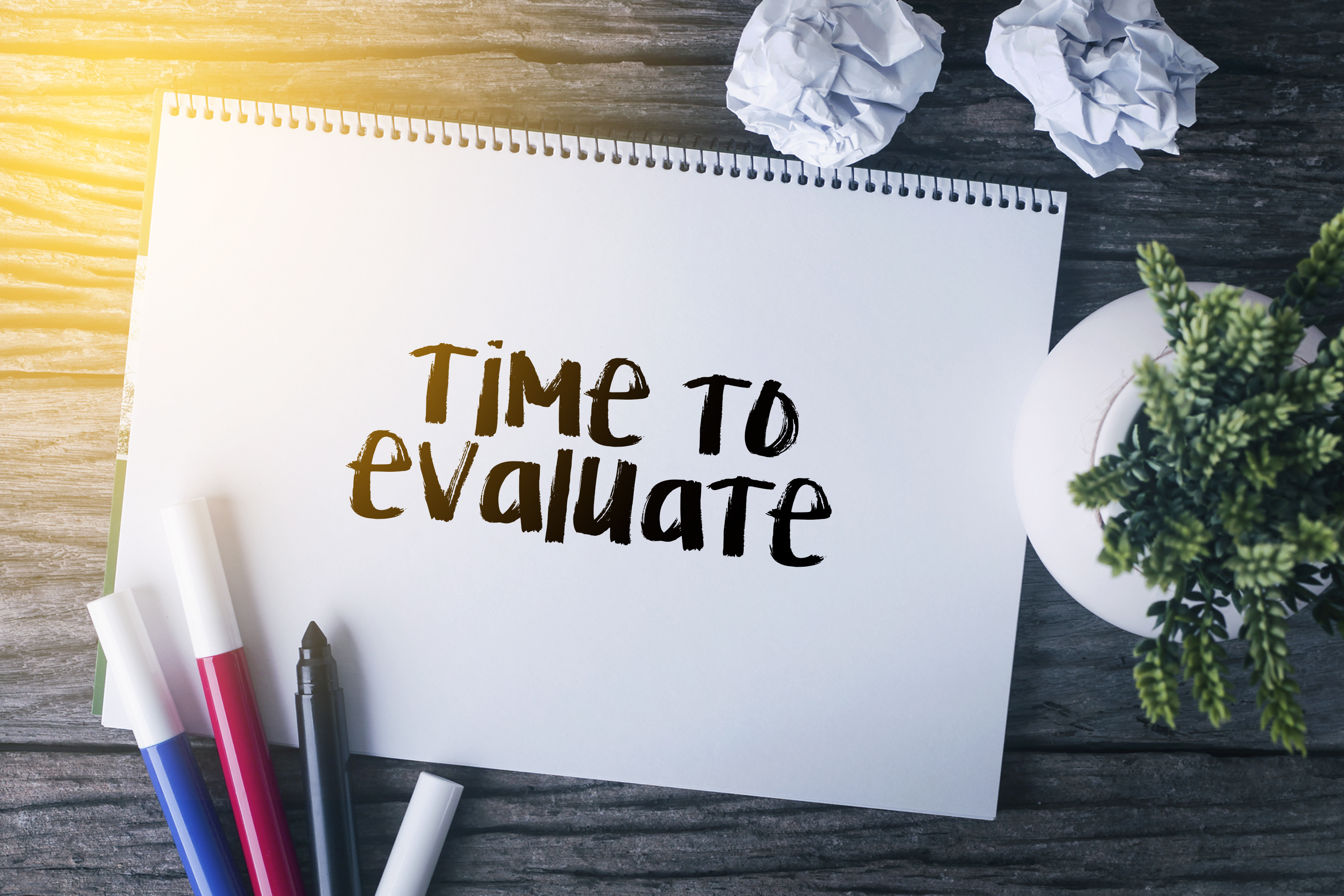 time-to-evaluate-word-with-notepad-and-green-plant-on-wooden-background