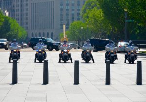 Police on motorcycles in front of SUVs in a motorcade