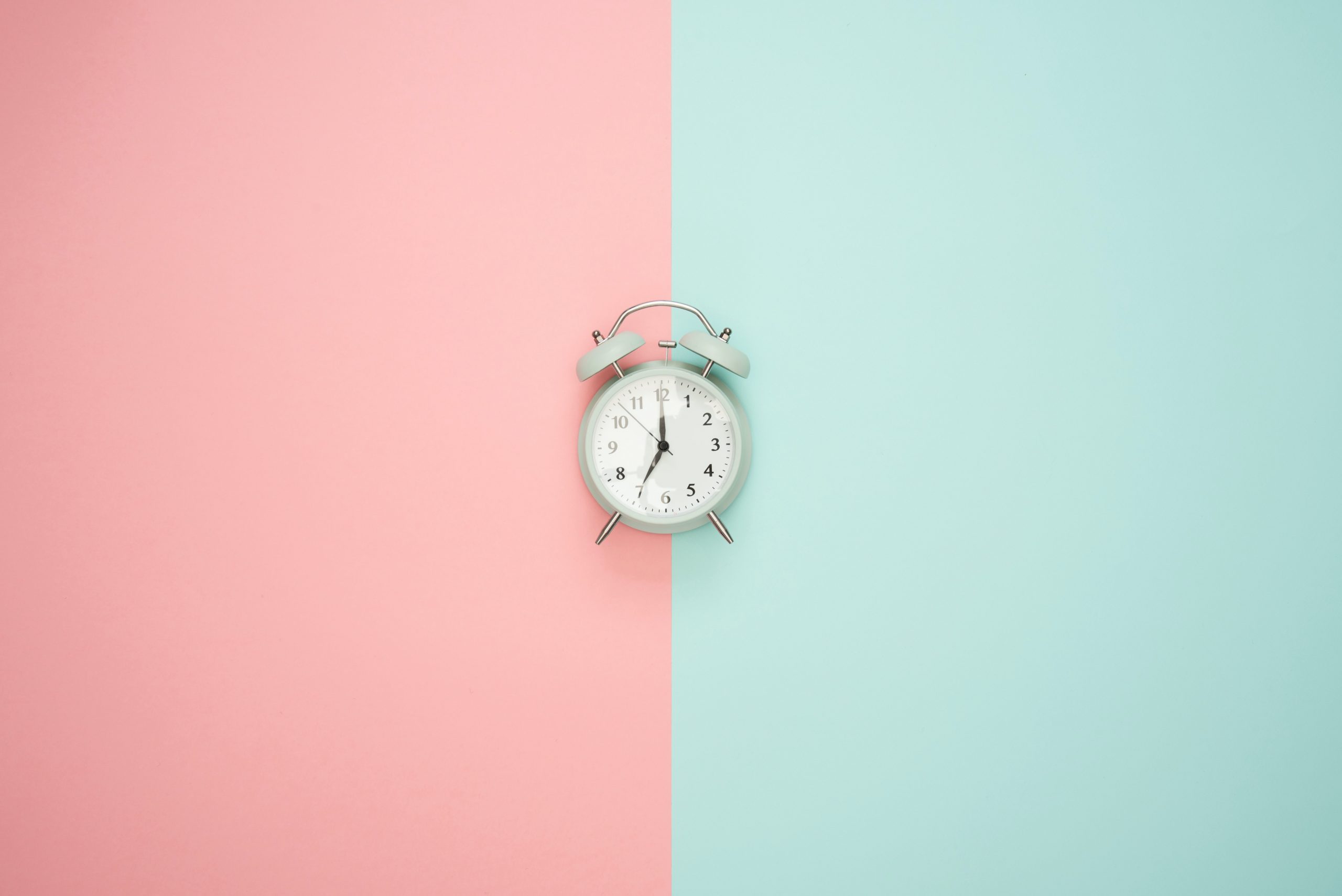 An alarm clock set against a pink and green backdrop