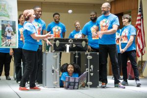 Group of people in blue shirts with young girl under luggage case