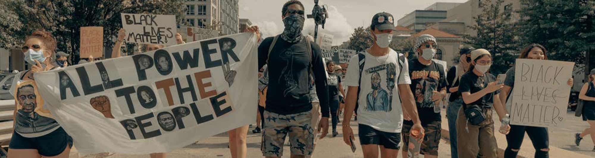 People wearing masks, marching in peace, holding signs that say "All the Power to the People" and "Black Lives Matter"