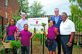 Group of smiling faces of different ethnicities and presenting genders standing in front of community garden