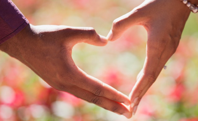 Two hands forming a heart with a floral background.