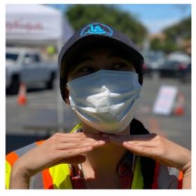 Woman posing with her hands under her chin in a face mask and baseball hat