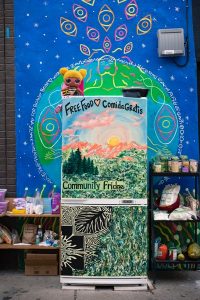 Painted community fridge in front of a mural of the Earth.