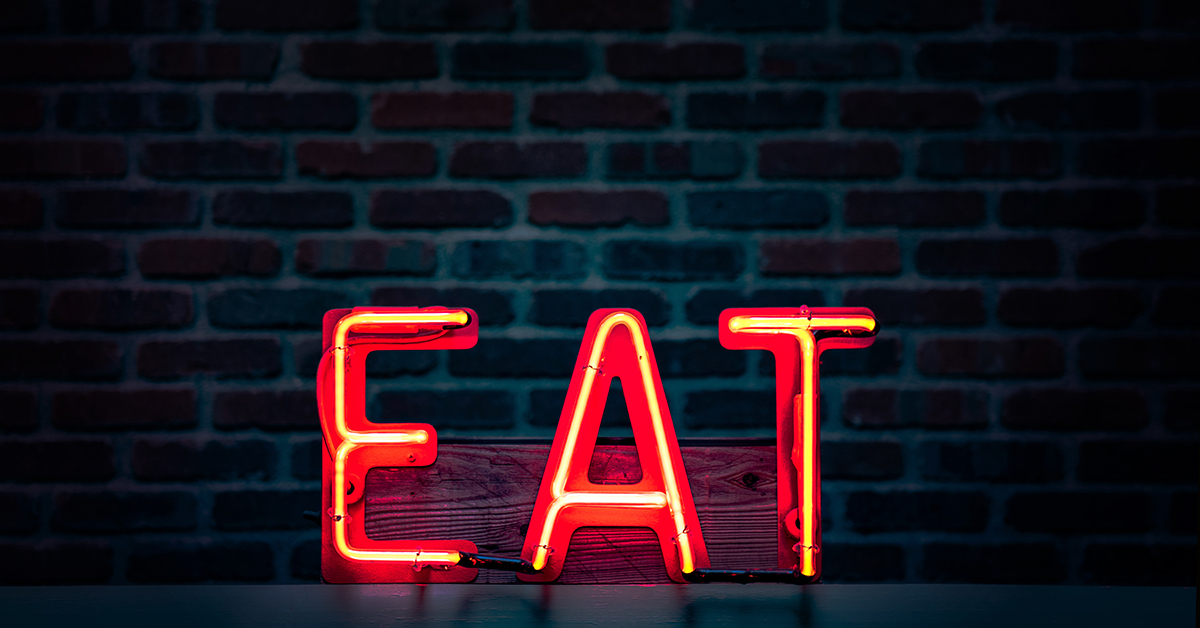 A red neon sign of the word "Eat" against a brick backdrop in a darkened room.