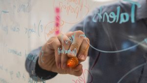 person writing on clear whiteboard