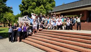 Several dozen people standing on steps next to City of San Rafael City Hall sign. Sky is blue.