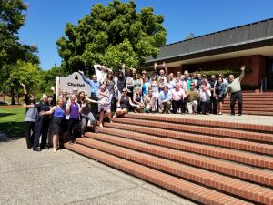 Several dozen people standing on steps next to City of San Rafael City Hall sign. Sky is blue.