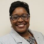 Headshot of black woman with short dark hair and glasses wearing a colorful top and light gray blazer.