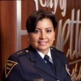 Headshot of brown skinned woman with short dark hair, in a police uniform.