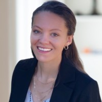 Headshot of light skinned woman with long brown hair, halfway pulled back, wearing a light colored top and dark blazer.