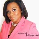 A headshot of a black woman with short dark hair, wearing a pink suit and strand of pearls, standing against a white background