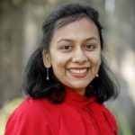 Headshot of Asian woman with shoulder length dark hair, wearing a red top and standing outside.