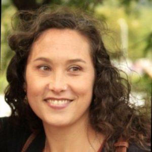 Portrait of light skinned woman with dark wavy hair past her shoulders, posing outside.