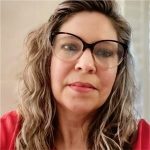 Headshot of white woman with long, wavy blond hair, glasses, and wearing a red top.