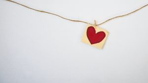 Piece of twine across a white background, with a tiny paperclip holding a small paper with a red heart on it.