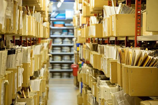 File room with a narrow walkway between tall shelf units filled with file-filled boxes.