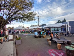 A scene of a city street lined with trees and pop-up tents. Chalk art is visible on the asphalt.