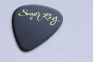 A black guitar pick emblazoned with the logo of the band Sugar Ray.