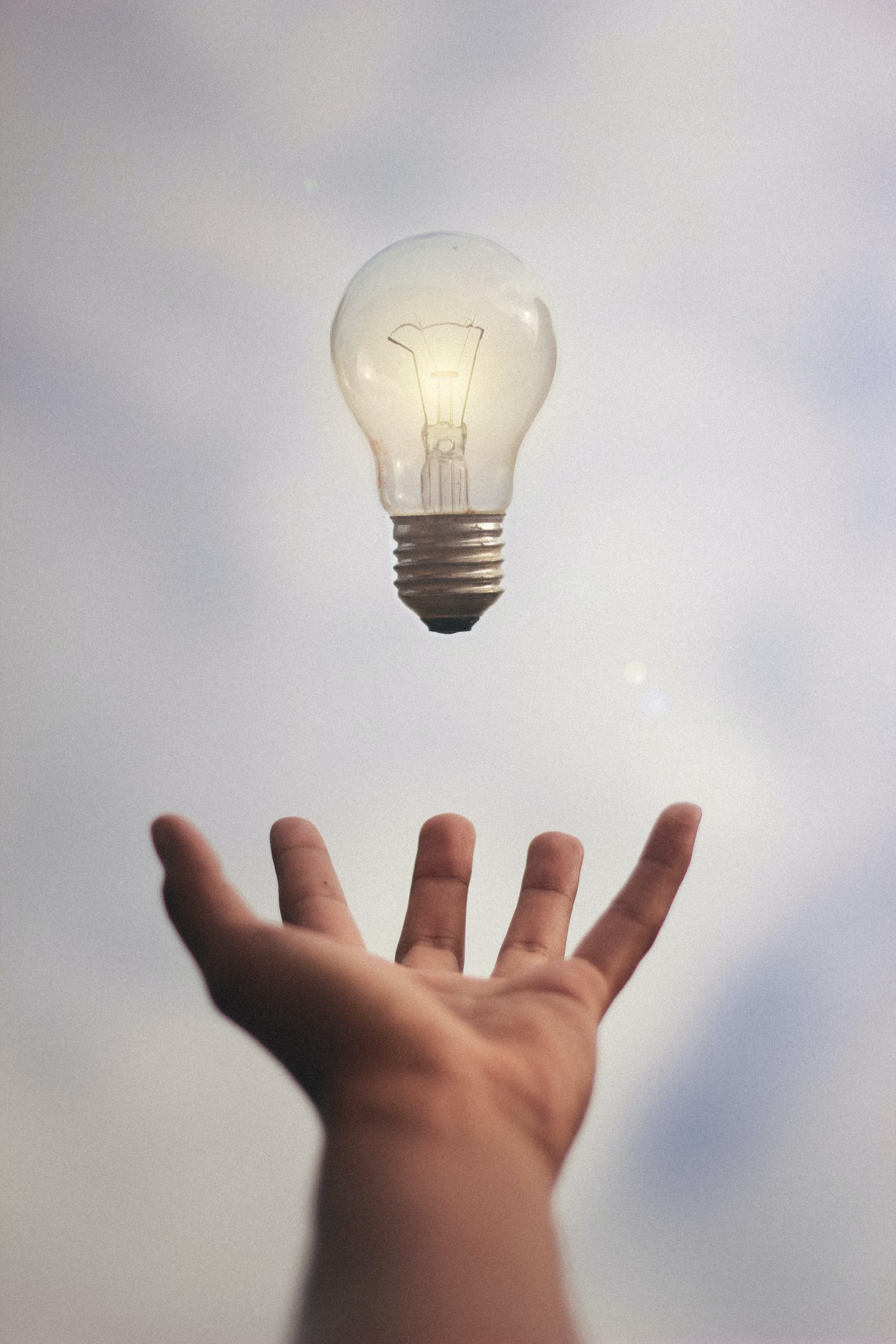 A hand reaches out to grasp a light bulb floating in space.