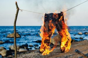 Clothesline on a beach with water in the background. Pants are hanging from the line and they are fully on fire.