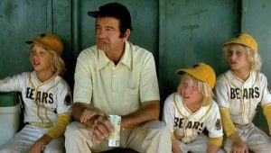 Walter Matthau sitting in a dugout with three blond-haired kids in Bears uniforms, from The Bad News Bears.