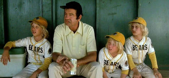 Walter Matthau sitting in a dugout with three blond-haired kids in Bears uniforms, from The Bad News Bears.