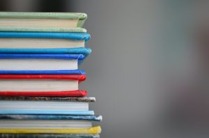 A stack of books with different colors of covers and spines sits against a grey background.