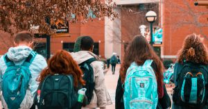 A group of students wearing backpacks is shown from behind as the group crosses a plaza.