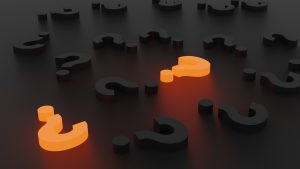 A series of three-dimensional black question marks lie against a black background, with two of the question marks glowing orange from within.