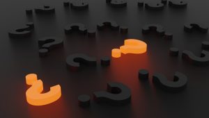 A series of three-dimensional black question marks lie against a black background, with two of the question marks glowing orange from within.