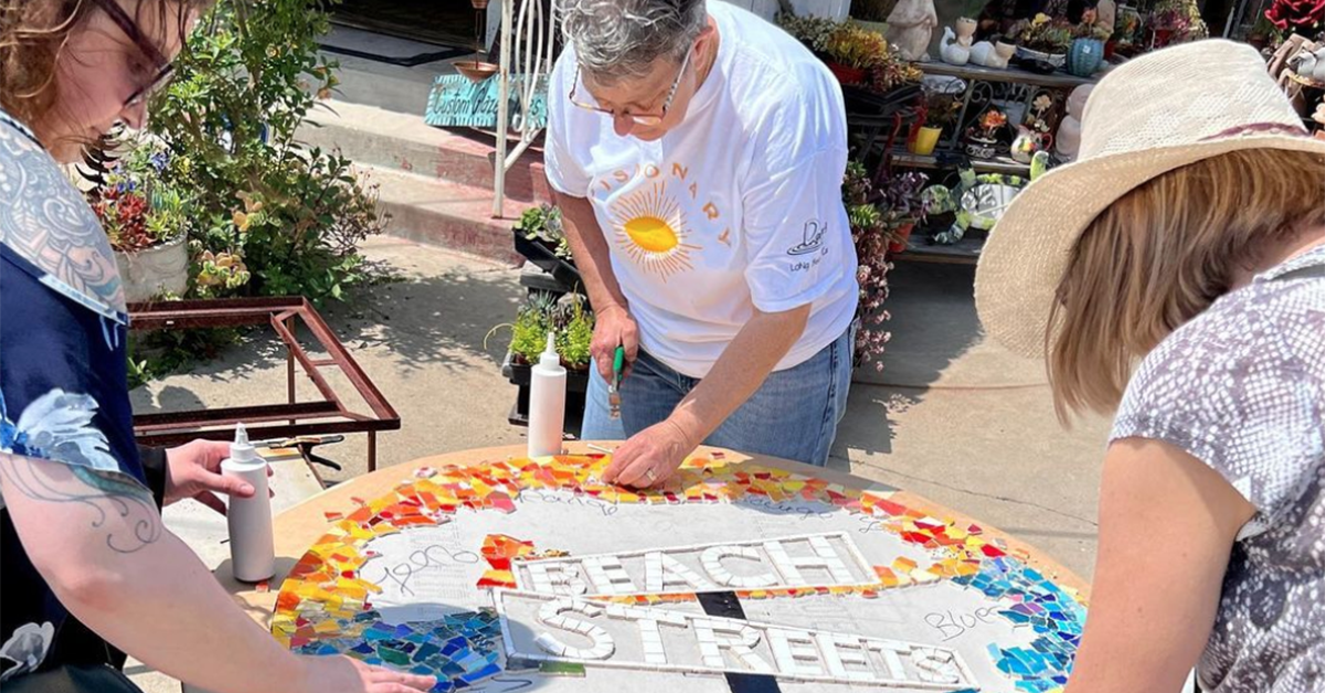 A group of people stand at a round table. Letters on the table spell out "Beach Streets."