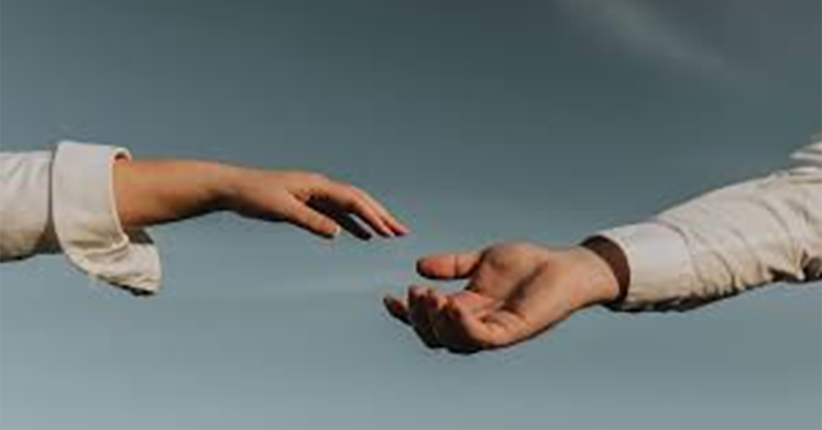 Two hands reaching out to clasp each other against a background of blue-gray sky.