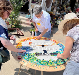 Three people around a table outside, creating a colorful mosaic that says Beach Streets in the middle.