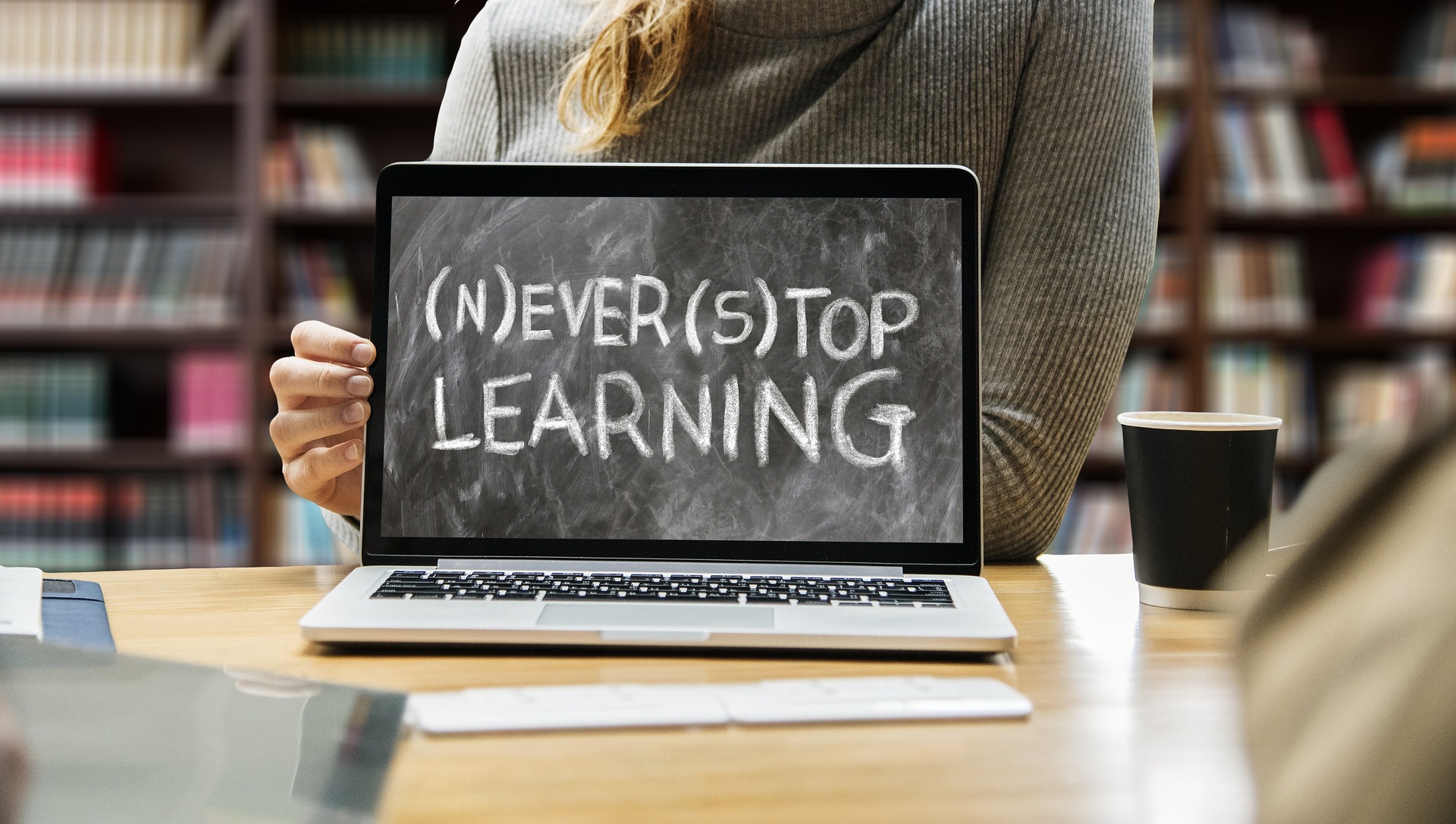 A person sits behind a laptop where the words (N)ever(S)top Learning appear on the screen.