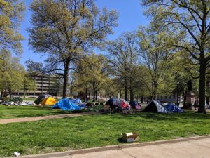 A group of camping tents beneath trees in a city park.