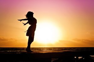 A profile silhouette of a woman standing with her arms outstretched against a rising sun.