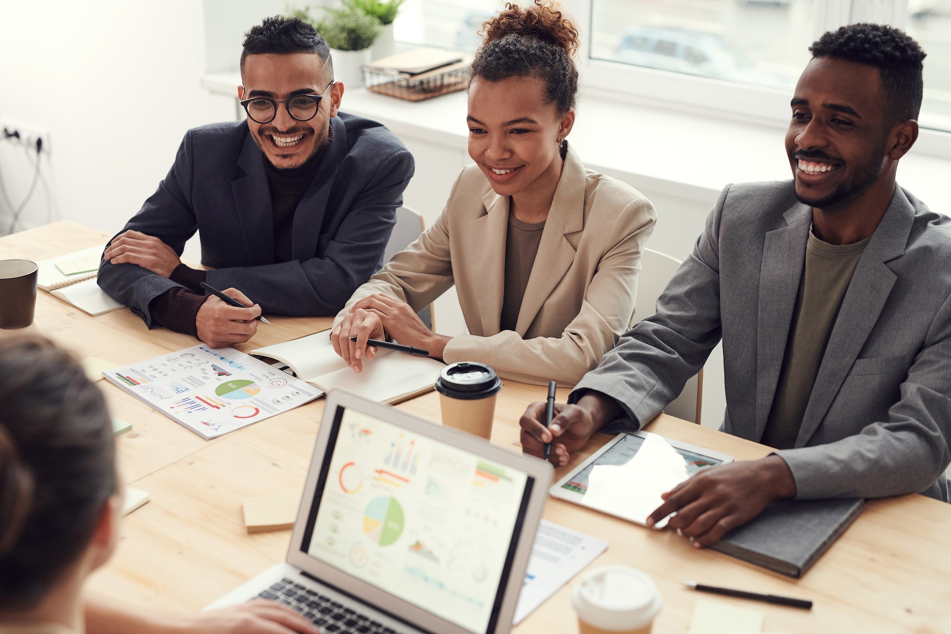 Three people in business suits sitting at a conference room table across from a person on a laptop.