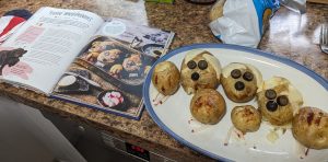 Kitchen countertop with cookbook open to baked potato recipe that looks like three-headed dog, with platter of completed recipe next to it.