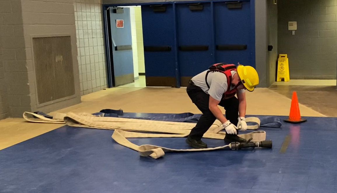 A person in firefighter gear rolls up a fire-fighting hose.