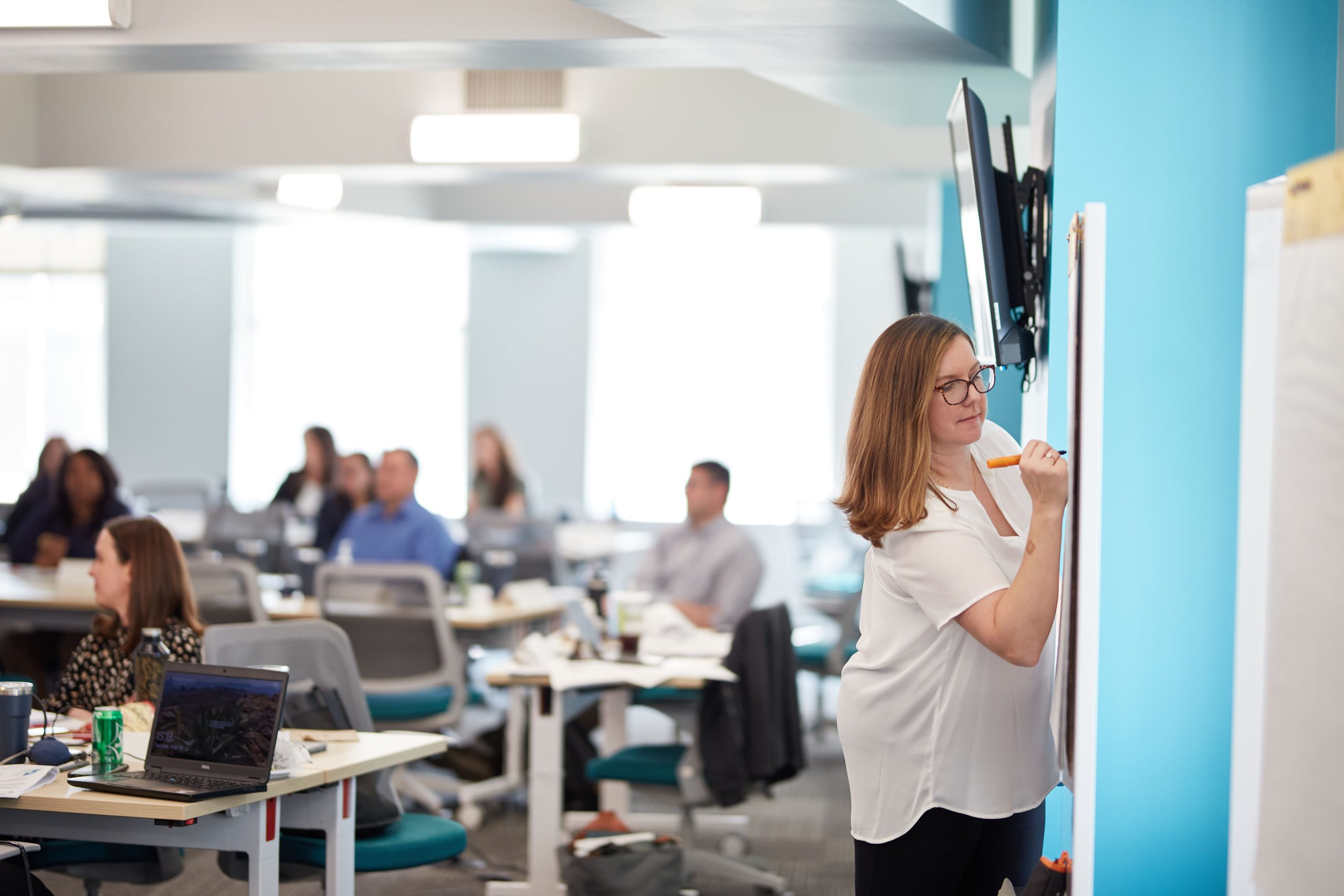 A woman writes on a whiteboard in front of a class.