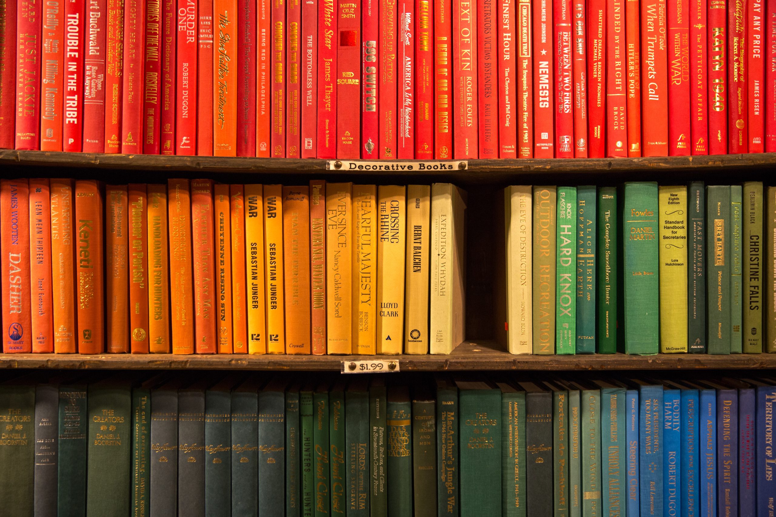 Three shelves filled with books in rainbow color order. Photo by Jason Leung on Unsplash.