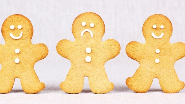 Three gingerbread people standing next to each other, with the two on the sides smiling and the middle one frowning.