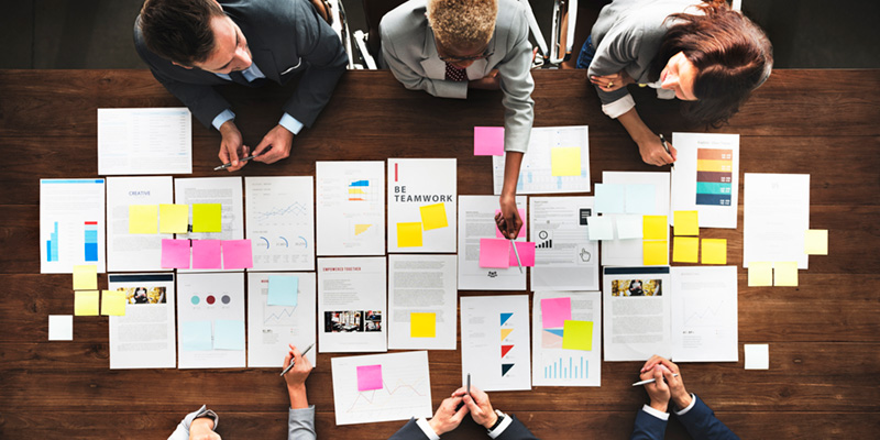 Overhead shot of people gathered around a conference table that is covered in multicolored sheets of paper.